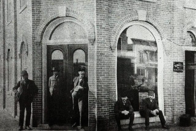 5 men in front of a brick bank building from the 1880s